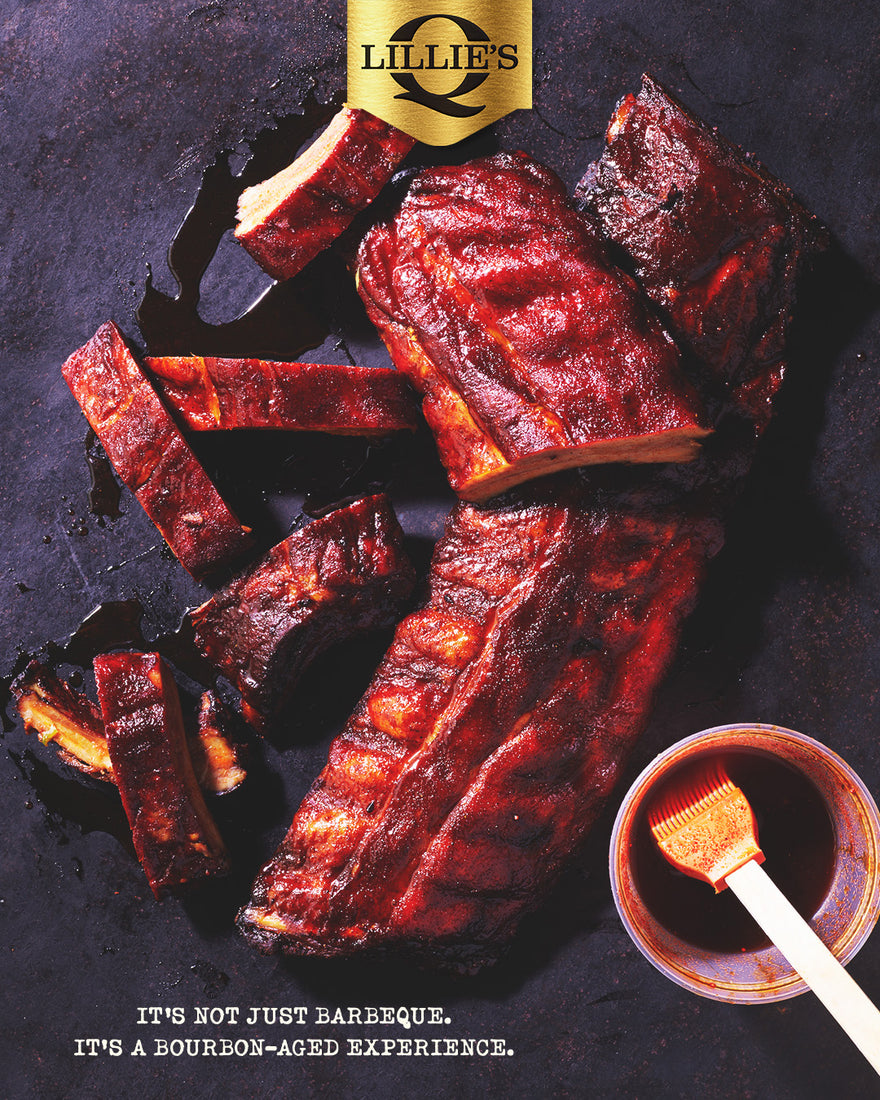 A top-down food advertisement showing glazed barbecue ribs on a dark surface, with a small cup of sauce and brush in the lower right and a gold Lillie's logo at the top. Text at the bottom reads, 'IT'S NOT JUST BARBEQUE.